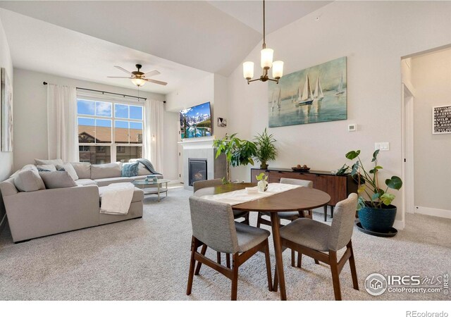 carpeted dining area with ceiling fan with notable chandelier, vaulted ceiling, and a tiled fireplace