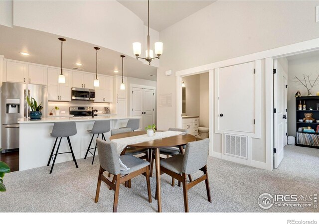 carpeted dining space featuring high vaulted ceiling and a chandelier