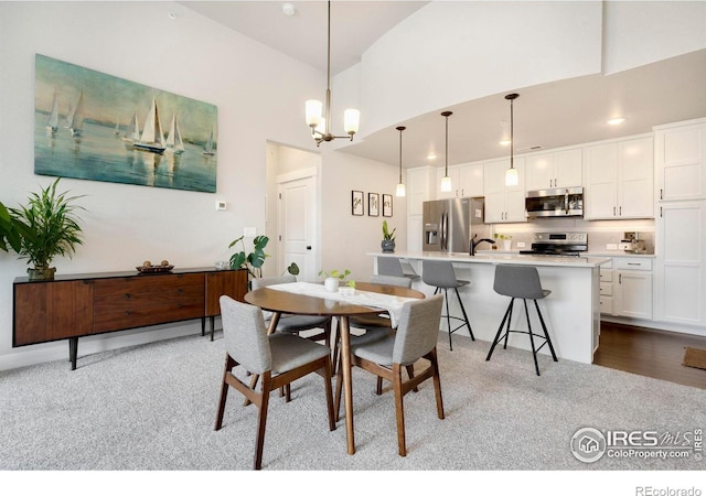 dining area featuring sink, an inviting chandelier, a high ceiling, and light wood-type flooring