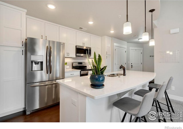 kitchen featuring visible vents, a sink, appliances with stainless steel finishes, white cabinetry, and a kitchen breakfast bar