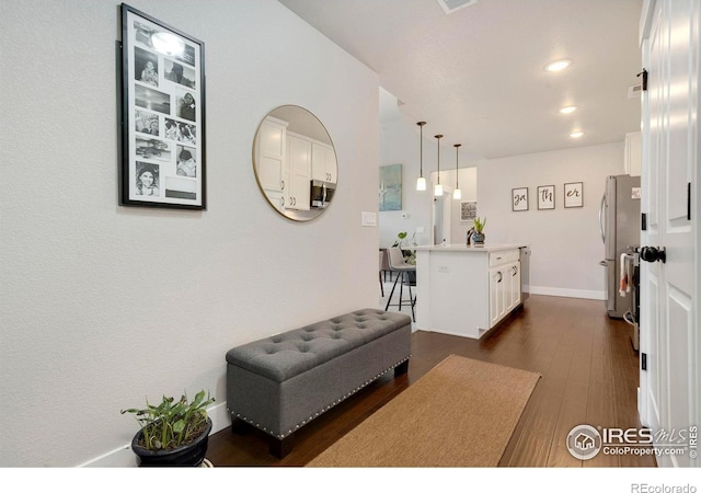 kitchen featuring dark wood-type flooring, hanging light fixtures, stainless steel fridge, an island with sink, and white cabinetry