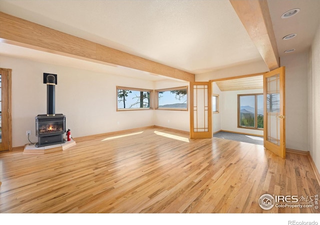 unfurnished living room with beamed ceiling, light hardwood / wood-style flooring, a wood stove, and french doors