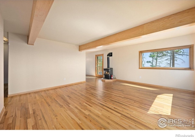 unfurnished living room featuring beamed ceiling, light hardwood / wood-style floors, and a wood stove