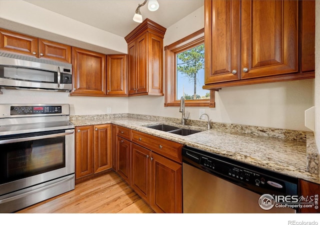 kitchen with sink, light stone countertops, light wood-type flooring, and stainless steel appliances