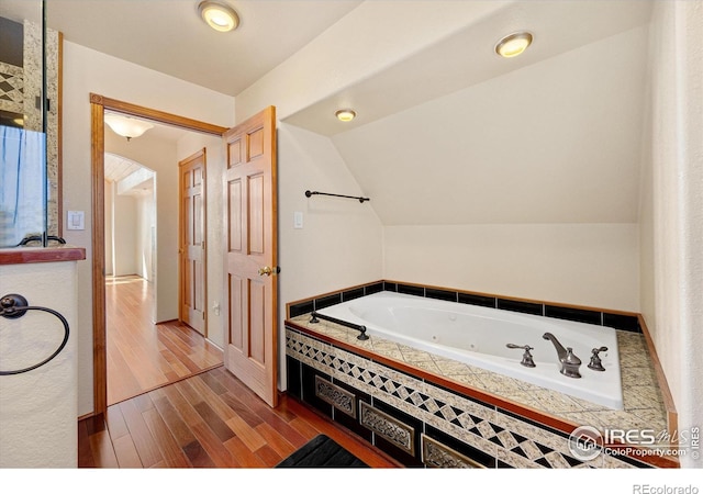 bathroom featuring tiled tub, wood-type flooring, and vaulted ceiling