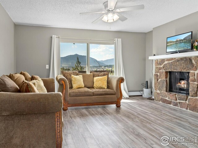 living room with light wood-type flooring, a textured ceiling, a baseboard heating unit, ceiling fan, and a fireplace