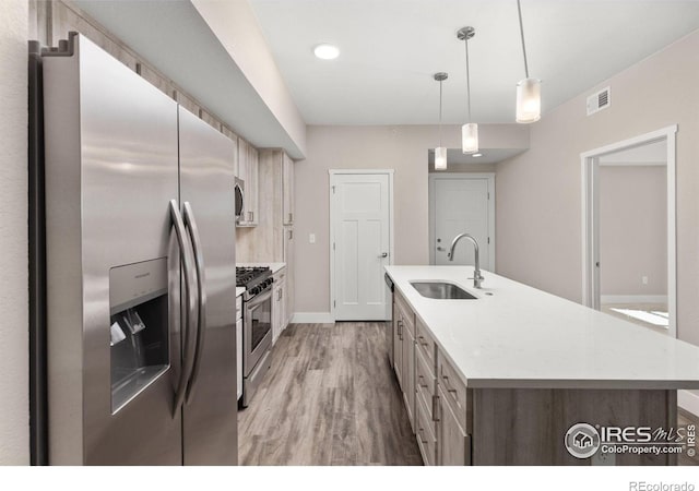 kitchen featuring appliances with stainless steel finishes, light wood-type flooring, an island with sink, pendant lighting, and sink