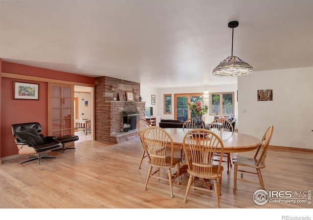 dining area featuring brick wall, light hardwood / wood-style flooring, a fireplace, and french doors