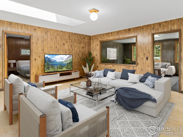 living room with a skylight, wooden walls, and light wood-style floors