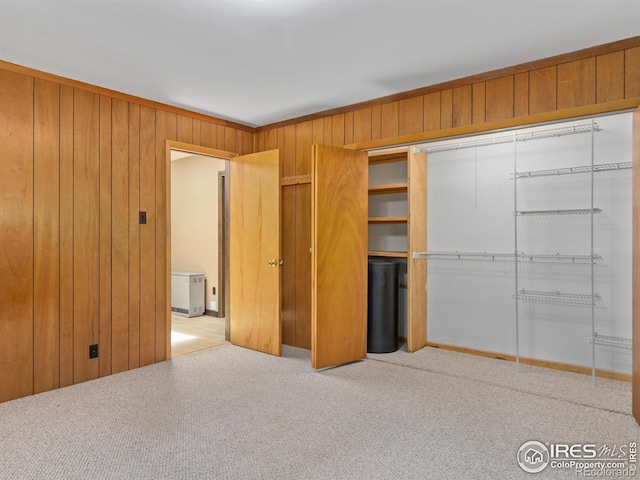 unfurnished bedroom featuring wood walls, a closet, and light colored carpet