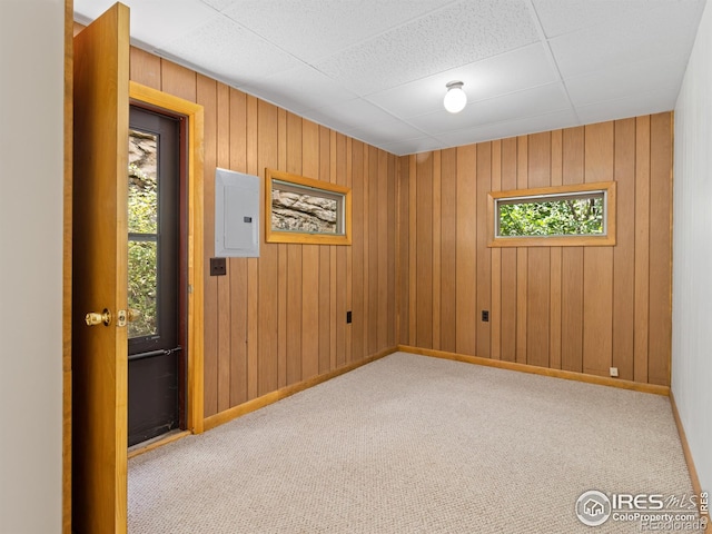 unfurnished room featuring light carpet, wood walls, electric panel, and baseboards