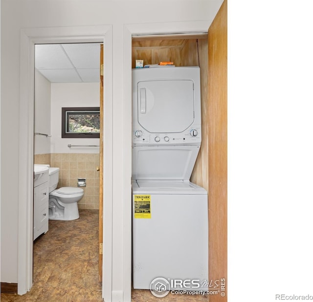 clothes washing area with stacked washing maching and dryer, tile walls, and wainscoting