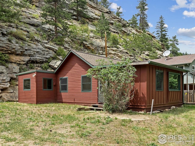 view of side of home featuring board and batten siding, roof with shingles, and a lawn