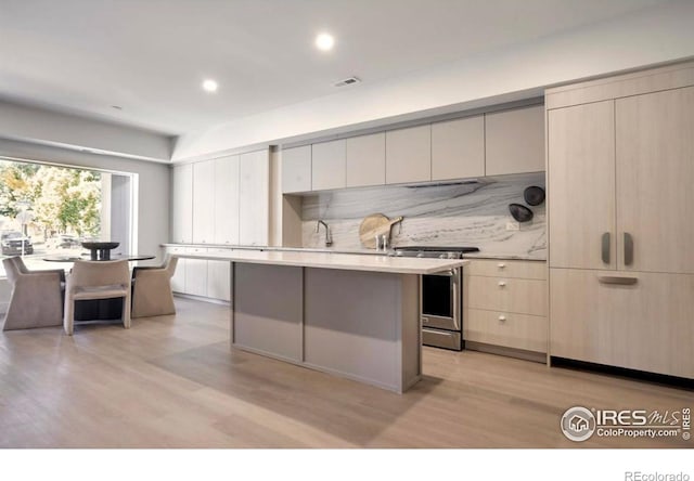 kitchen with light hardwood / wood-style floors, a center island, tasteful backsplash, sink, and stainless steel range