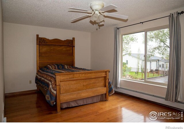 bedroom featuring a textured ceiling, light hardwood / wood-style flooring, ceiling fan, and baseboard heating