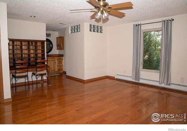 empty room with ceiling fan, a textured ceiling, hardwood / wood-style floors, and a baseboard radiator