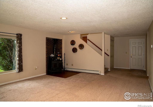 unfurnished living room featuring a baseboard radiator, a wood stove, carpet floors, and a textured ceiling