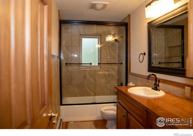 full bathroom with a baseboard heating unit, vanity, shower / bath combination with glass door, and toilet