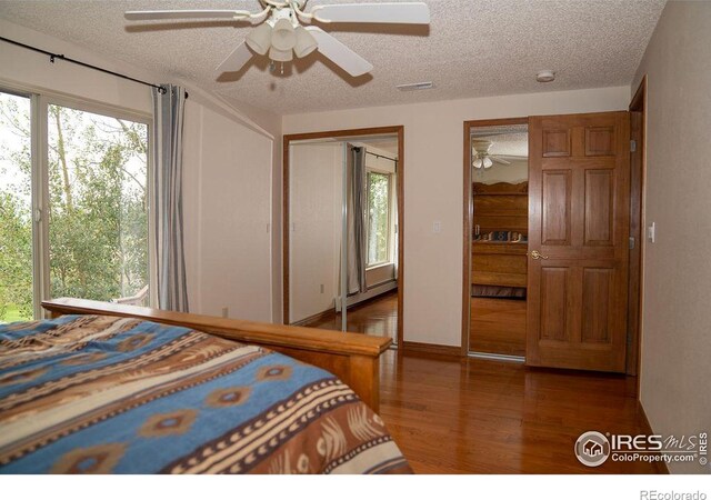 bedroom featuring ceiling fan, baseboard heating, multiple windows, and wood-type flooring