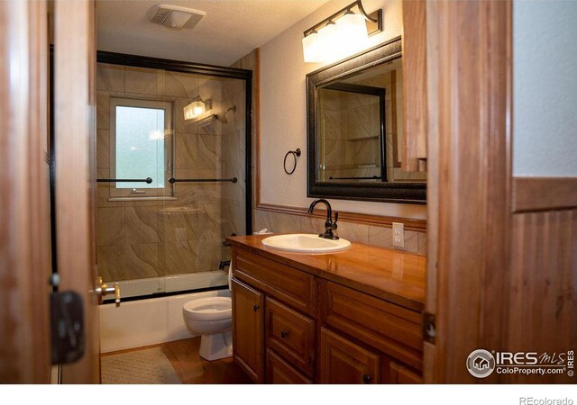 full bathroom featuring a textured ceiling, toilet, bath / shower combo with glass door, and vanity