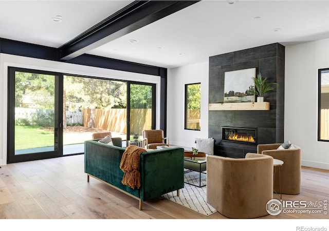 living room with beamed ceiling, a large fireplace, and light hardwood / wood-style floors