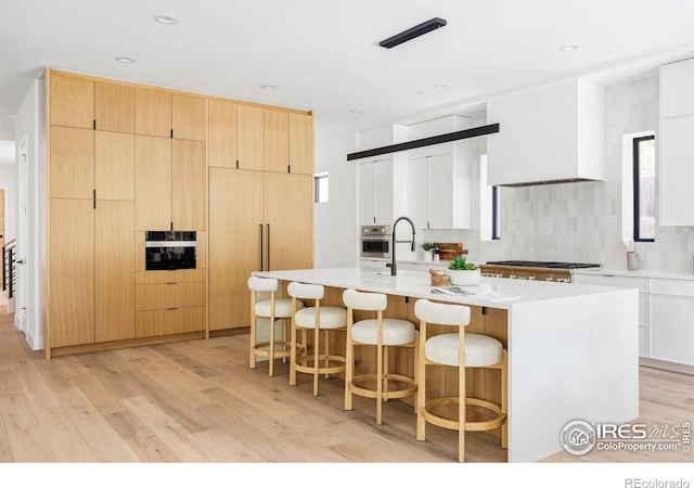 kitchen with light hardwood / wood-style flooring, stainless steel appliances, an island with sink, and white cabinets