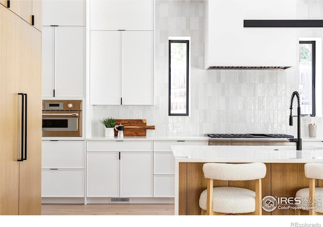 kitchen with white cabinets, backsplash, oven, and a kitchen breakfast bar