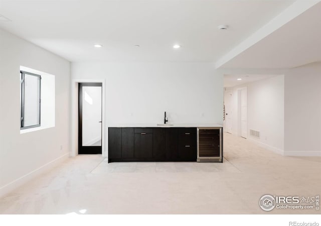 bar with dark brown cabinets, sink, light colored carpet, and beverage cooler