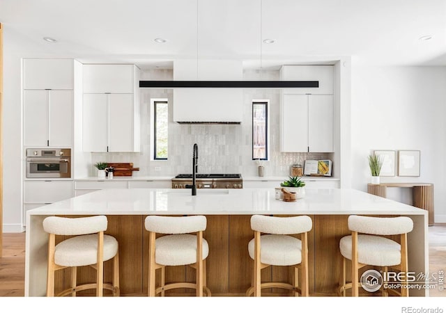 kitchen with white cabinetry, light hardwood / wood-style flooring, oven, and an island with sink