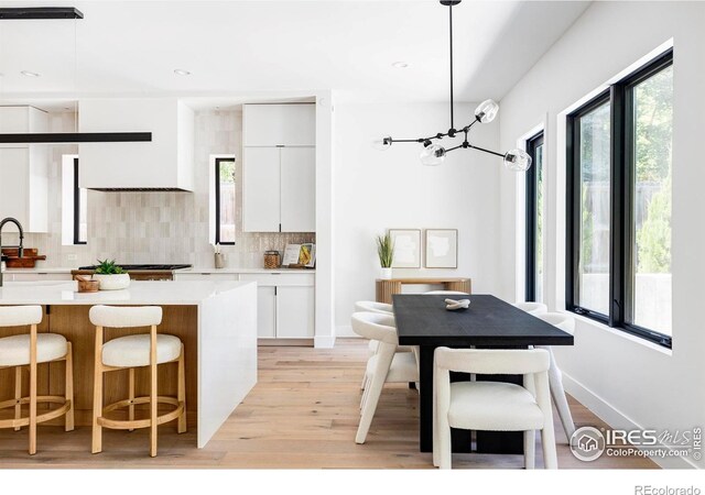 kitchen with sink, white cabinetry, tasteful backsplash, hanging light fixtures, and light hardwood / wood-style flooring