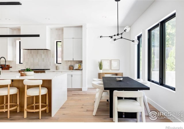 kitchen featuring sink, white cabinets, decorative backsplash, hanging light fixtures, and light hardwood / wood-style floors