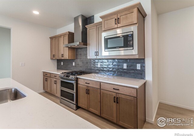 kitchen with appliances with stainless steel finishes, light hardwood / wood-style flooring, wall chimney range hood, and decorative backsplash