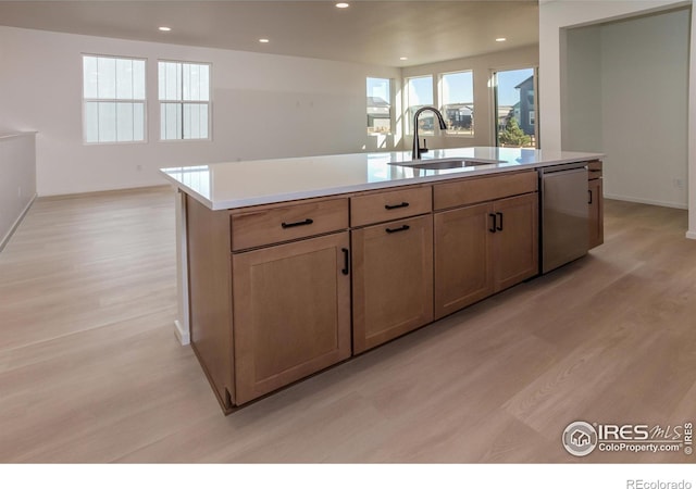 kitchen featuring stainless steel dishwasher, light hardwood / wood-style floors, sink, and a center island with sink