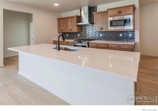 kitchen featuring sink, light hardwood / wood-style flooring, a center island with sink, appliances with stainless steel finishes, and wall chimney range hood