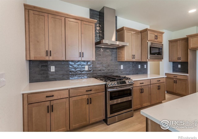 kitchen featuring tasteful backsplash, wall chimney range hood, light wood-type flooring, and appliances with stainless steel finishes