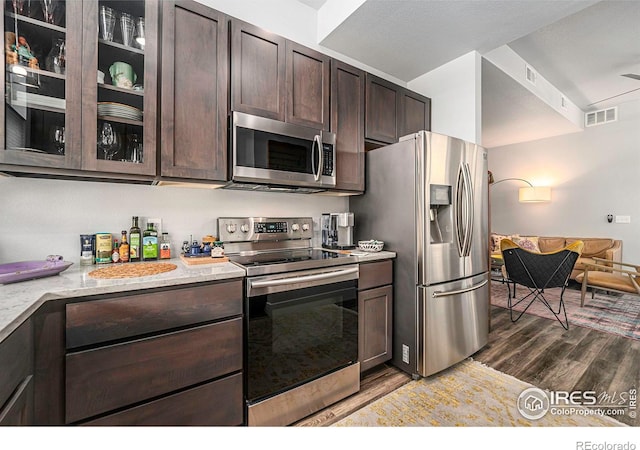 kitchen with visible vents, glass insert cabinets, dark brown cabinetry, appliances with stainless steel finishes, and wood finished floors