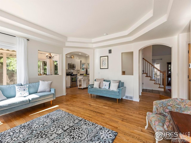 living room with a chandelier, a raised ceiling, and light wood-type flooring