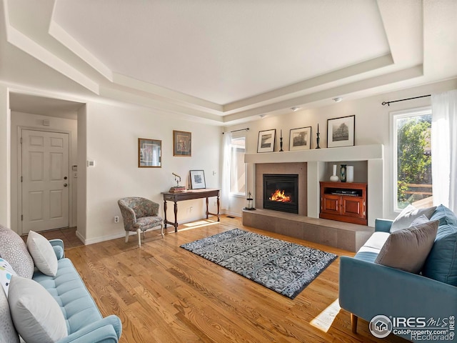 living room with a tray ceiling, a fireplace, and light wood-type flooring