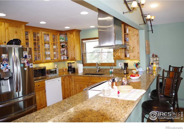 kitchen with appliances with stainless steel finishes, a breakfast bar area, light stone countertops, sink, and wall chimney range hood