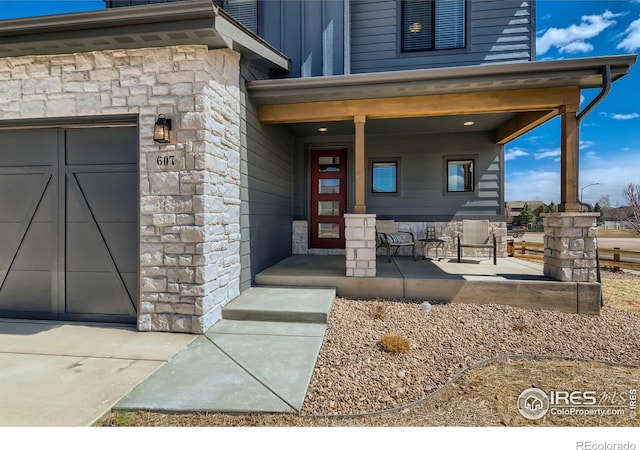 property entrance featuring covered porch, stone siding, board and batten siding, and a garage