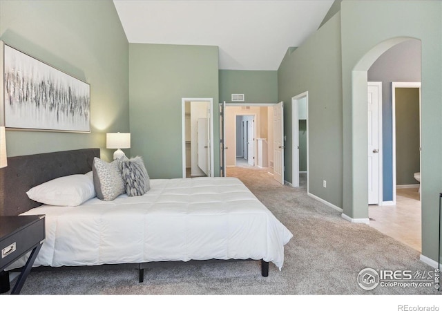 carpeted bedroom with connected bathroom and high vaulted ceiling