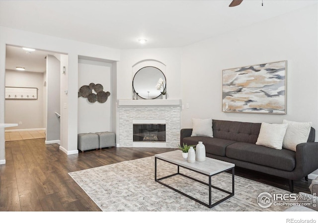 living room with ceiling fan, dark hardwood / wood-style flooring, and a stone fireplace