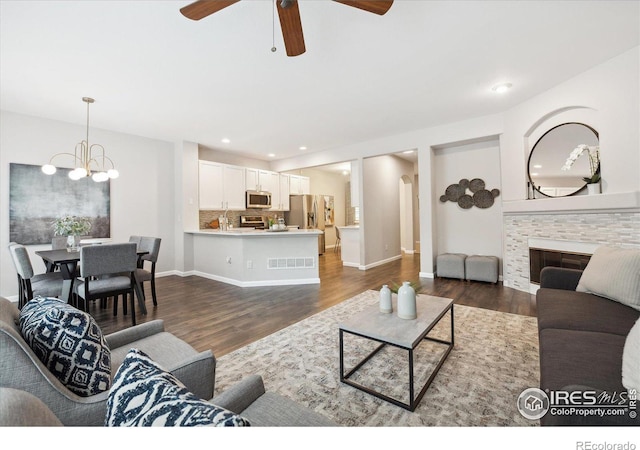 living room with ceiling fan with notable chandelier, a fireplace, and dark hardwood / wood-style flooring