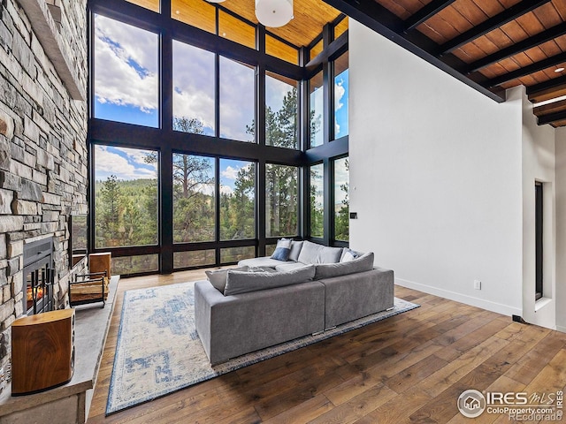 living room featuring wooden ceiling, high vaulted ceiling, a stone fireplace, and hardwood / wood-style flooring