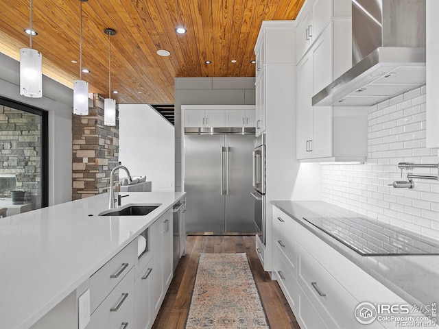 kitchen with dark hardwood / wood-style floors, appliances with stainless steel finishes, wall chimney range hood, decorative light fixtures, and tasteful backsplash