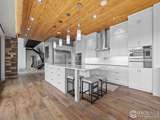 kitchen with tasteful backsplash, wood-type flooring, wall chimney range hood, and an island with sink