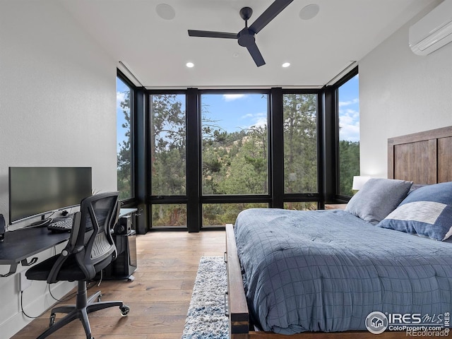 bedroom with an AC wall unit, ceiling fan, a wall of windows, and light hardwood / wood-style floors