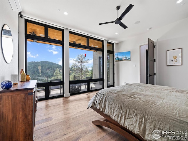 bedroom featuring light wood-type flooring, floor to ceiling windows, a wall mounted AC, ceiling fan, and access to exterior