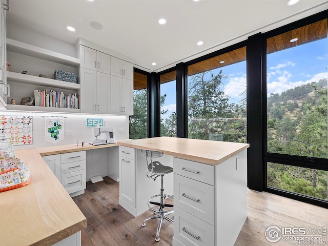 office featuring wood-type flooring, a wall of windows, plenty of natural light, and built in desk