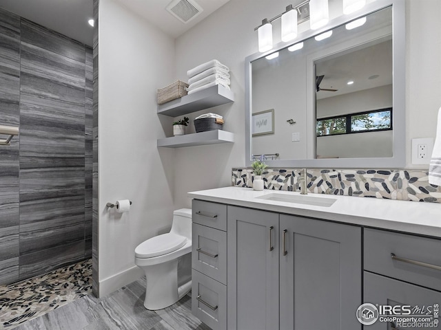 bathroom with toilet, tile patterned floors, a tile shower, vanity, and decorative backsplash